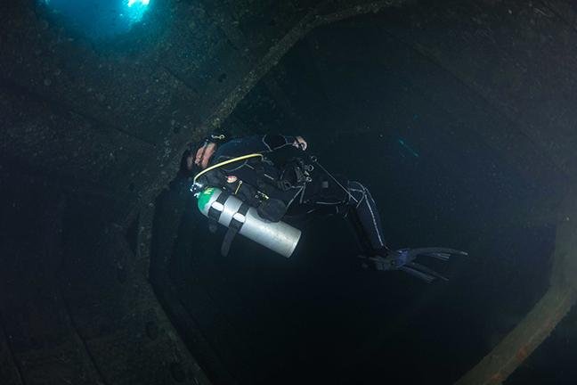 Diver with torch penetrating the dark interior of a Coron wreck