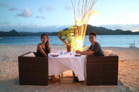 Couple at a candlelit table set on the sand at sunset