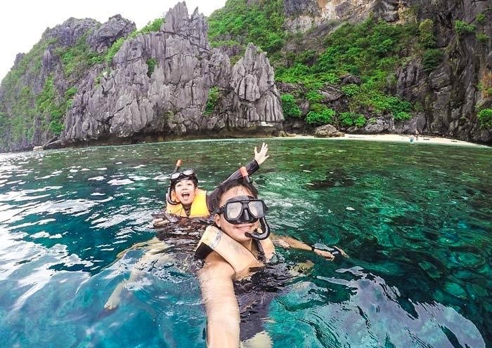 Couple snorkelling in clear shallow water below karst cliffs