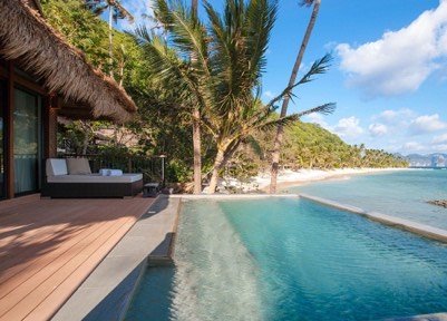 Resort pool and daybed beneath palms facing the beach