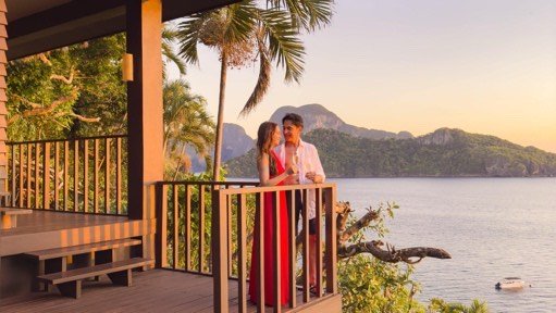 Couple on a villa balcony watching the sunset over the bay