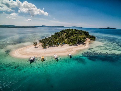 Aerial view of a small island with a white sandbar and moored boats