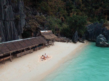 Couple on a quiet white sand beach beside a thatched shelter
