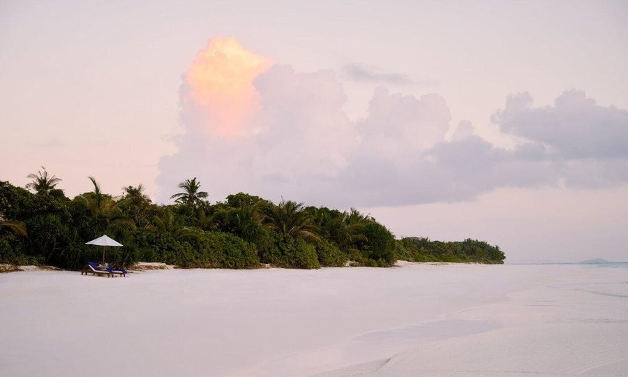 White-sand beach at dawn with a parasol and two loungers before the palm-covered length of Pamalican Island