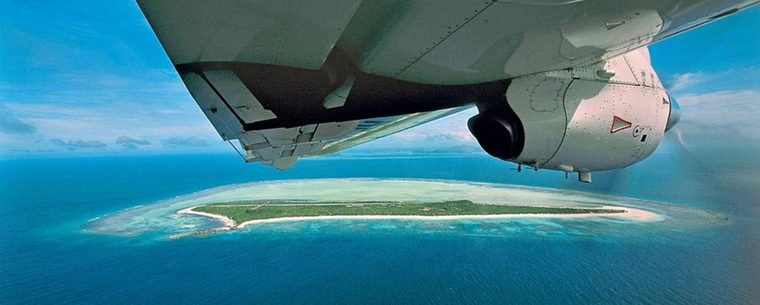 View past the wing of the charter aircraft down onto Pamalican Island ringed by reef and turquoise shallows