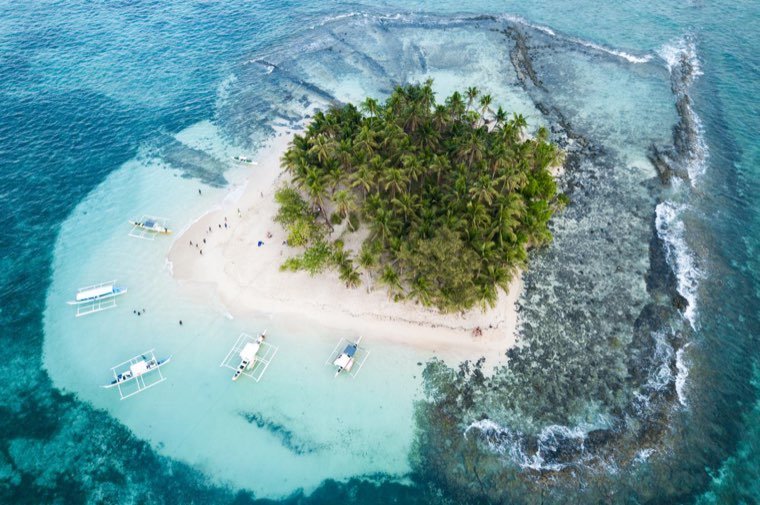 Aerial view of tiny palm-covered Guyam Island ringed by turquoise water