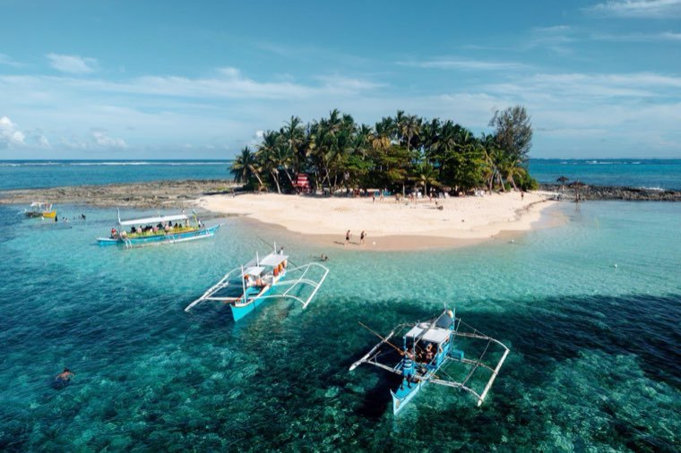 Outrigger boats and swimmers at a small tropical island near Siargao