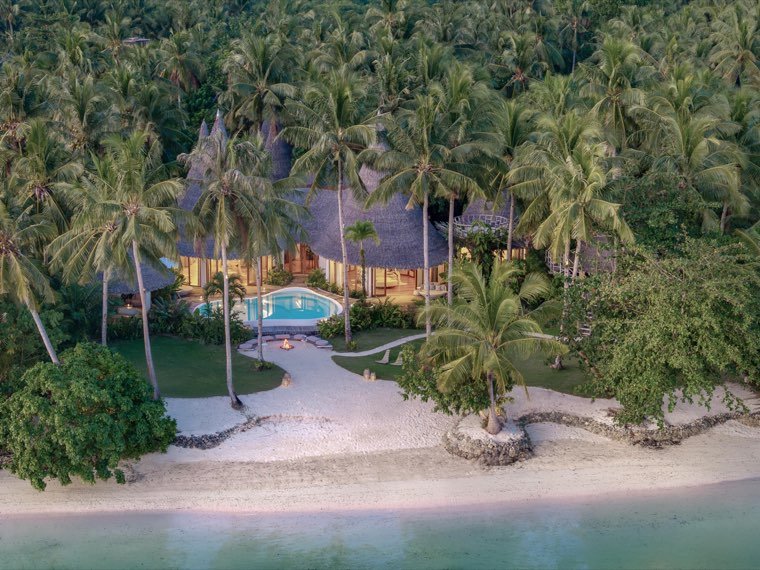 Resort pool and thatched pavilions among palms beside a white sand beach