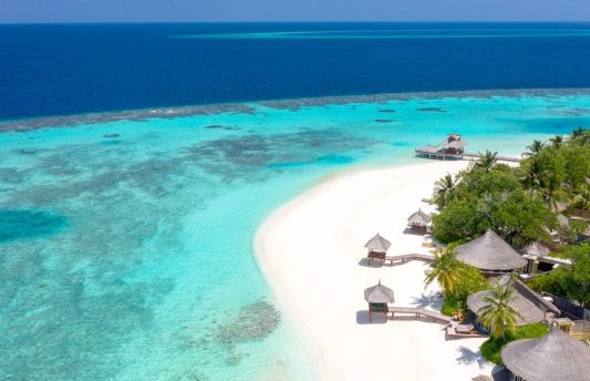 Aerial view of beachfront villa at Banyan Tree Vabbinfaru Maldives, surrounded by white sandy beaches, lush tropical vegetation, and crystal-clear turquoise waters of North Malé Atoll.